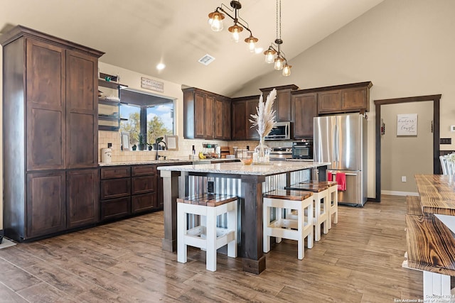 kitchen with decorative backsplash, appliances with stainless steel finishes, light wood-type flooring, pendant lighting, and lofted ceiling