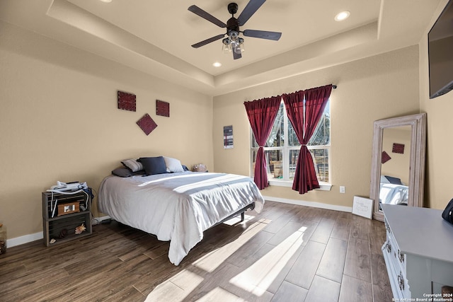 bedroom with dark hardwood / wood-style flooring, a raised ceiling, and ceiling fan