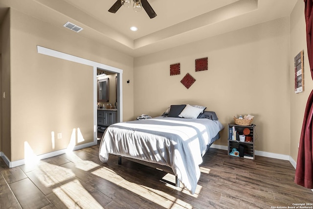 bedroom with wood-type flooring, ensuite bathroom, ceiling fan, and a tray ceiling