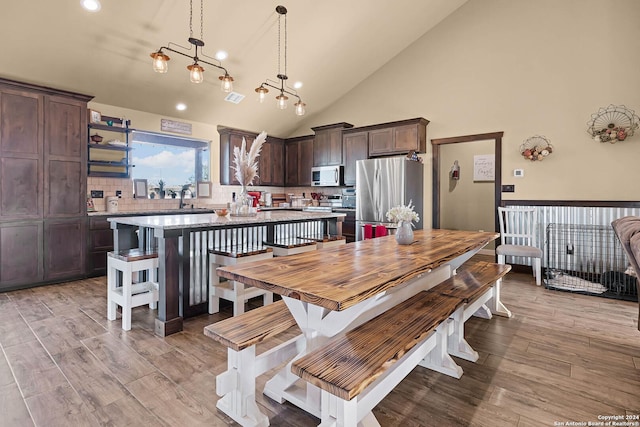 dining area with sink, high vaulted ceiling, light hardwood / wood-style floors, and a notable chandelier