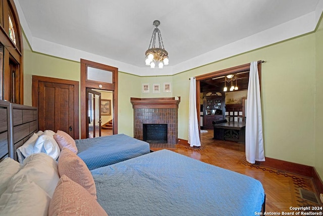 bedroom featuring a brick fireplace, an inviting chandelier, and parquet floors