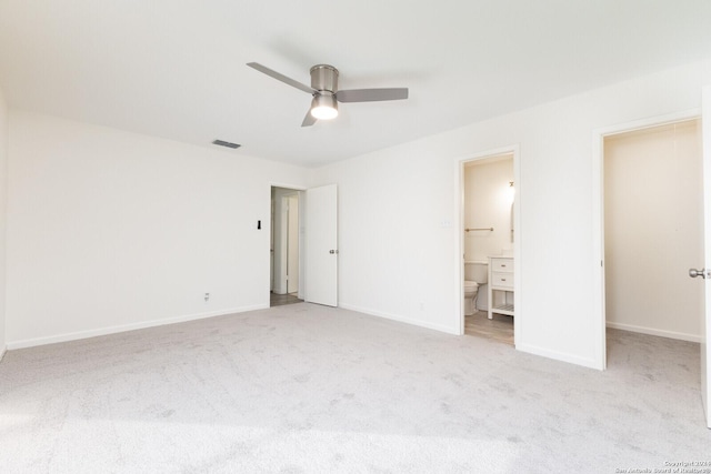 unfurnished bedroom with ceiling fan, a walk in closet, light carpet, and ensuite bath