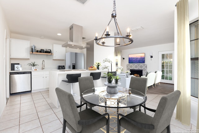 dining space featuring a tile fireplace, light tile patterned floors, an inviting chandelier, and sink