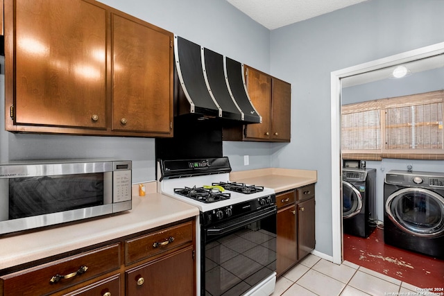 kitchen featuring extractor fan, white range with gas cooktop, washing machine and clothes dryer, stainless steel microwave, and light tile patterned flooring