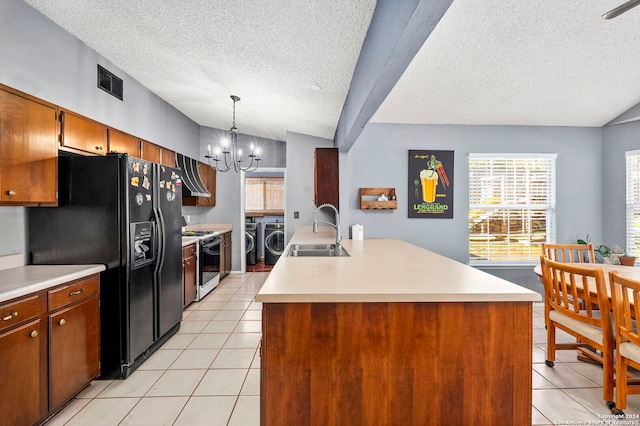 kitchen featuring gas range gas stove, sink, light tile patterned floors, a center island with sink, and washing machine and dryer