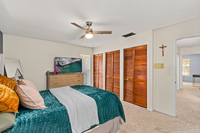 bedroom with carpet, a textured ceiling, two closets, and ceiling fan