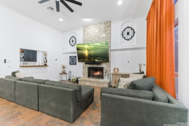 living room with a stone fireplace, ceiling fan, and ornamental molding