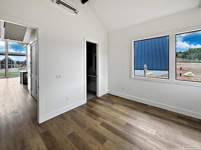 unfurnished bedroom featuring ensuite bath, a wall mounted AC, multiple windows, and hardwood / wood-style flooring