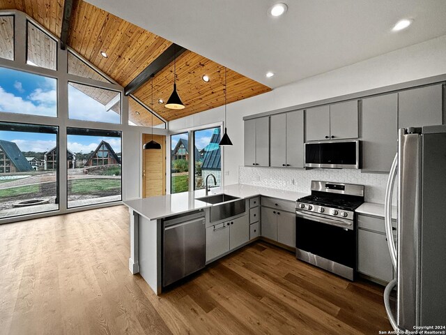 kitchen with kitchen peninsula, stainless steel appliances, sink, pendant lighting, and gray cabinets