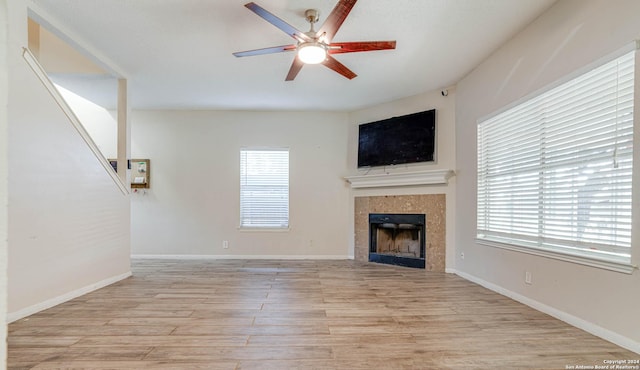 unfurnished living room featuring ceiling fan, a healthy amount of sunlight, light hardwood / wood-style floors, and a tile fireplace