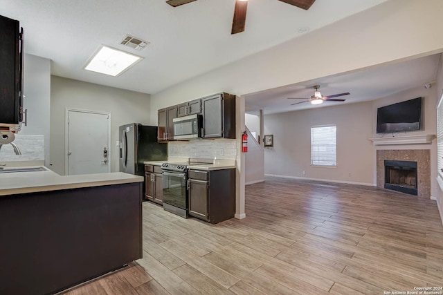 kitchen with a fireplace, light hardwood / wood-style flooring, dark brown cabinets, and appliances with stainless steel finishes