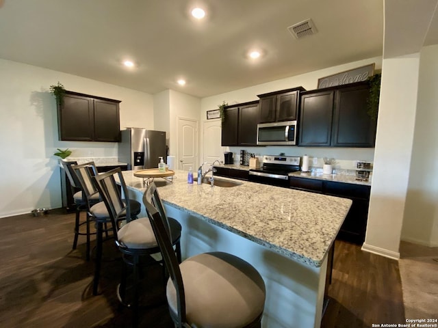 kitchen featuring light stone countertops, sink, dark wood-type flooring, a kitchen island with sink, and appliances with stainless steel finishes