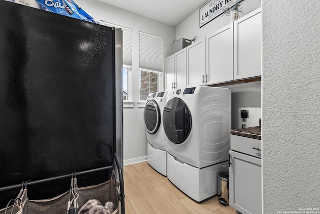 clothes washing area with washing machine and dryer, light hardwood / wood-style flooring, and cabinets