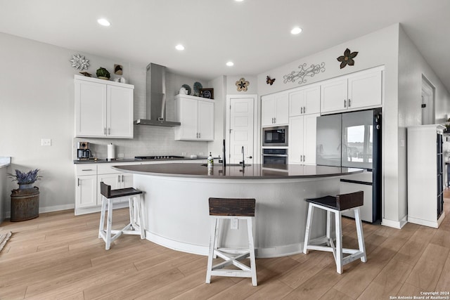 kitchen featuring a kitchen bar, wall chimney range hood, stainless steel appliances, and a kitchen island with sink