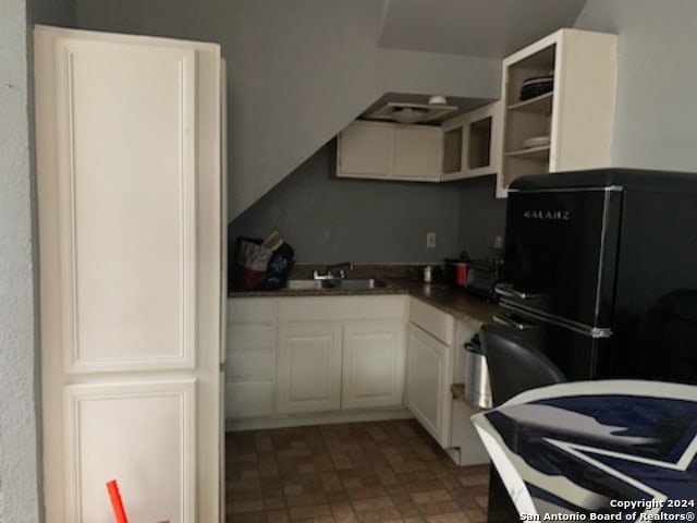 kitchen with black refrigerator, white cabinets, and sink