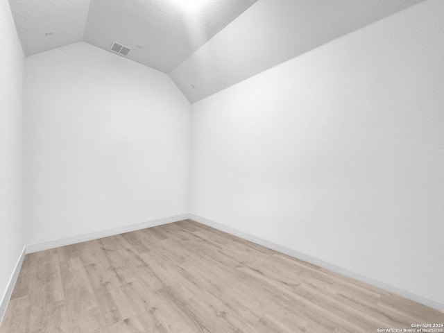 unfurnished room featuring a textured ceiling, light wood-type flooring, and lofted ceiling