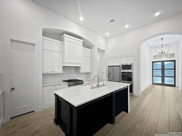 kitchen featuring stainless steel appliances, tasteful backsplash, a kitchen island with sink, white cabinets, and light wood-type flooring