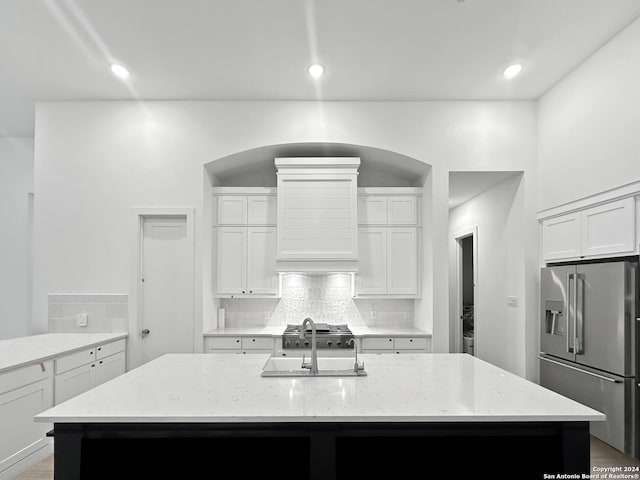 kitchen with stainless steel refrigerator with ice dispenser, light stone counters, sink, a center island with sink, and white cabinets