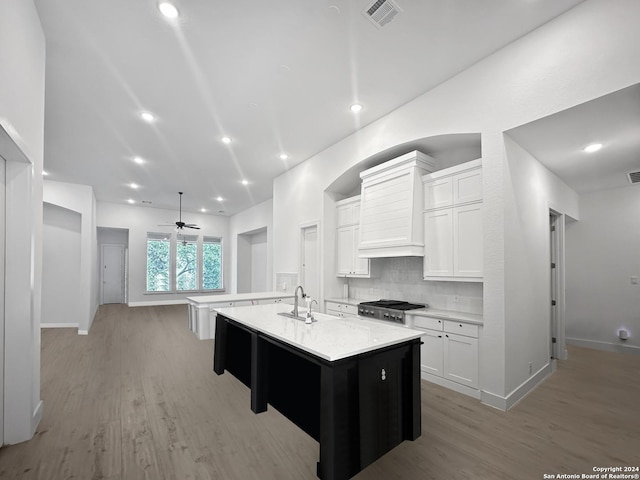 kitchen featuring light wood-type flooring, white cabinetry, a kitchen island with sink, and ceiling fan