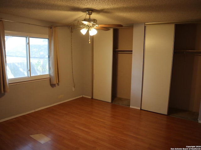 unfurnished bedroom with a textured ceiling, hardwood / wood-style flooring, ceiling fan, and multiple closets