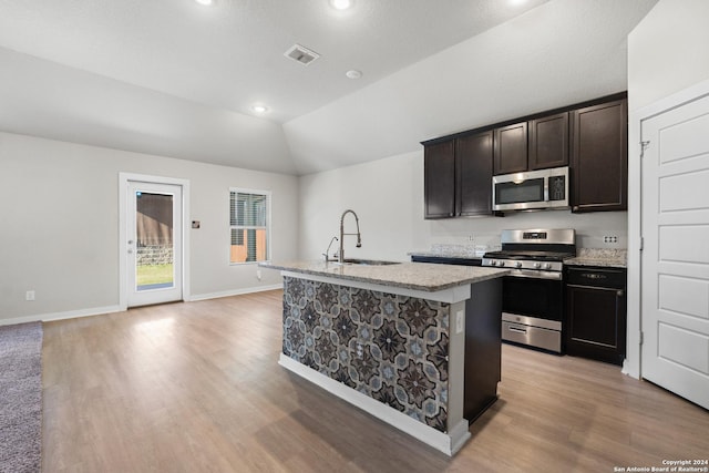 kitchen with a center island with sink, sink, light hardwood / wood-style flooring, vaulted ceiling, and appliances with stainless steel finishes