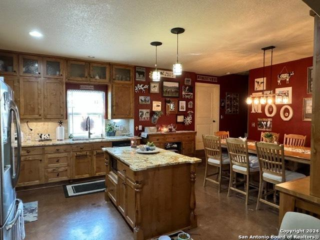 kitchen featuring stainless steel refrigerator, sink, a kitchen island, and hanging light fixtures