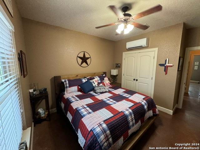 bedroom with a wall mounted AC, a textured ceiling, a closet, and ceiling fan