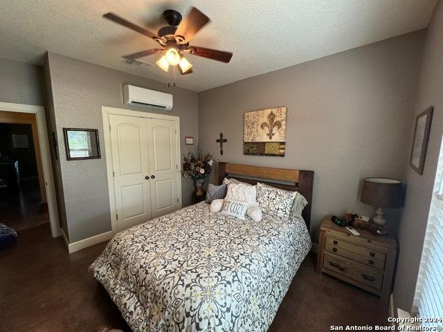 bedroom with a wall mounted AC, ceiling fan, a closet, and a textured ceiling