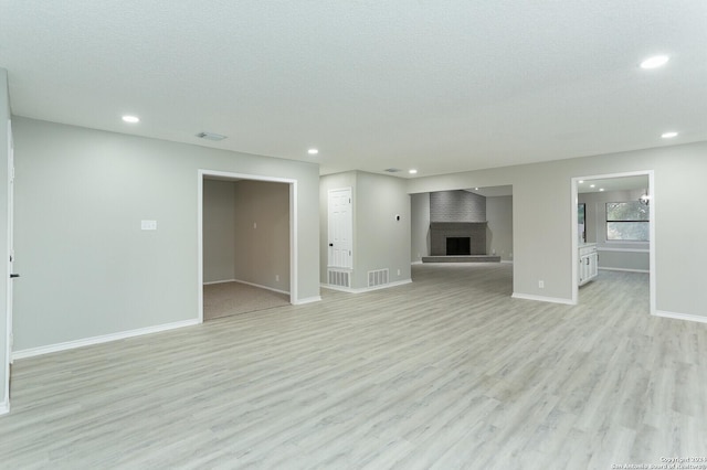 unfurnished living room featuring a large fireplace, light hardwood / wood-style flooring, and a textured ceiling