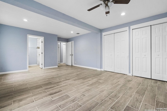 unfurnished bedroom featuring connected bathroom, light hardwood / wood-style floors, ceiling fan, and multiple closets