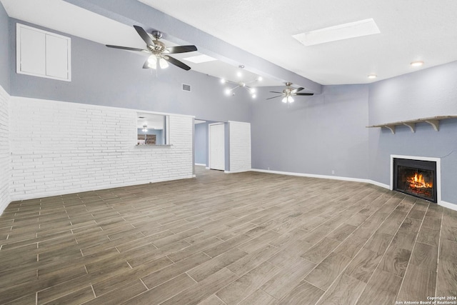 unfurnished living room with a skylight, hardwood / wood-style flooring, ceiling fan, and brick wall