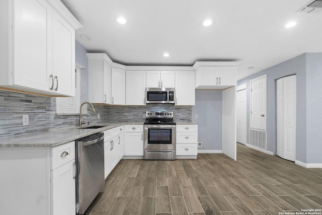 kitchen with light stone countertops, appliances with stainless steel finishes, sink, hardwood / wood-style flooring, and white cabinetry