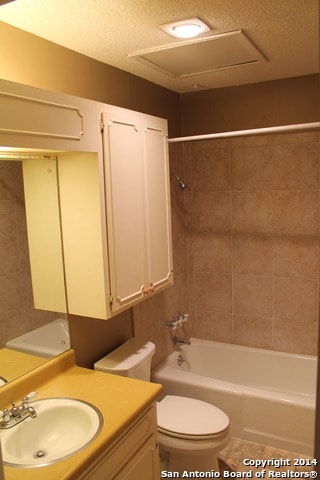 full bathroom featuring a textured ceiling, vanity, toilet, and tiled shower / bath