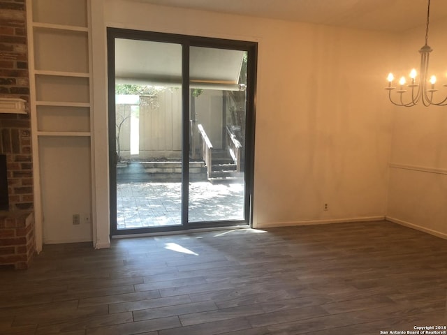 unfurnished room featuring dark hardwood / wood-style flooring, a fireplace, and an inviting chandelier