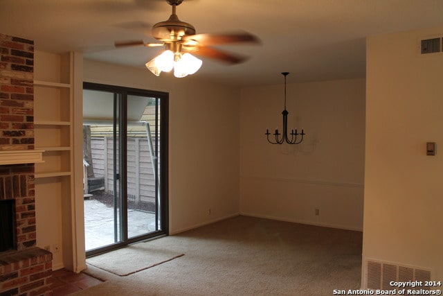 unfurnished dining area featuring carpet, ceiling fan with notable chandelier, and a brick fireplace