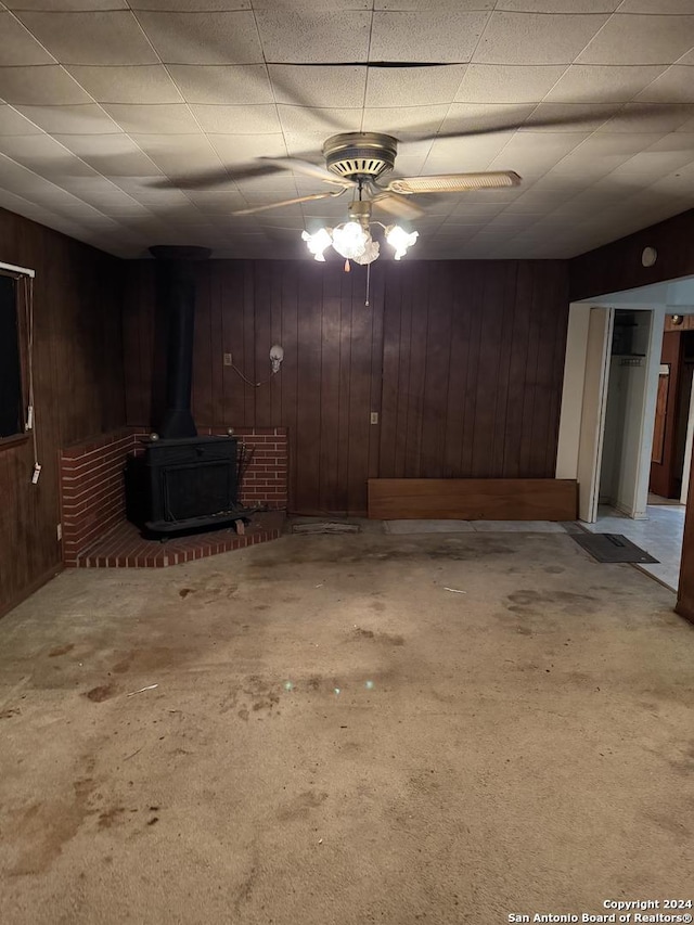 basement featuring a wood stove, ceiling fan, and wood walls