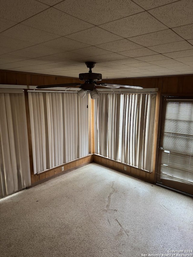 empty room with carpet floors, a drop ceiling, and wooden walls