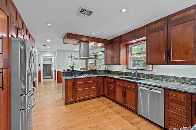 kitchen with dark stone countertops, light wood-type flooring, kitchen peninsula, island exhaust hood, and stainless steel appliances