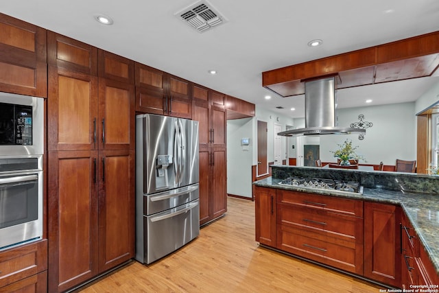 kitchen featuring island range hood, dark stone countertops, light wood-type flooring, and appliances with stainless steel finishes