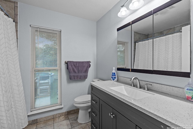 bathroom with tile patterned floors, a wealth of natural light, vanity, and toilet