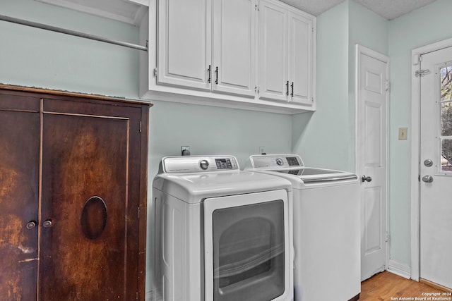 laundry room with washing machine and dryer, cabinets, a textured ceiling, and light hardwood / wood-style floors