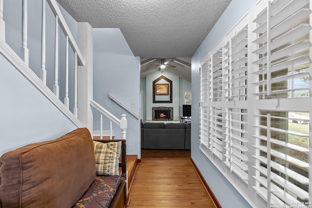 hall with a textured ceiling, light hardwood / wood-style floors, and lofted ceiling