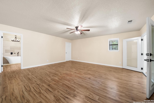 empty room with ceiling fan with notable chandelier, wood-type flooring, and a textured ceiling