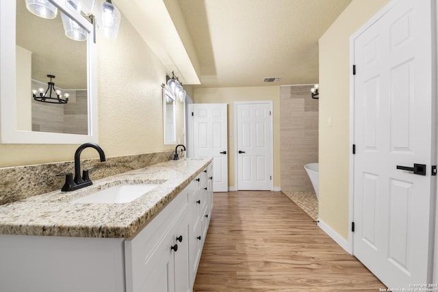 bathroom with vanity, a bath, an inviting chandelier, hardwood / wood-style flooring, and a textured ceiling