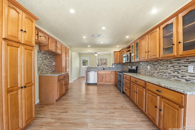 kitchen with ceiling fan, light wood-type flooring, appliances with stainless steel finishes, light stone counters, and kitchen peninsula