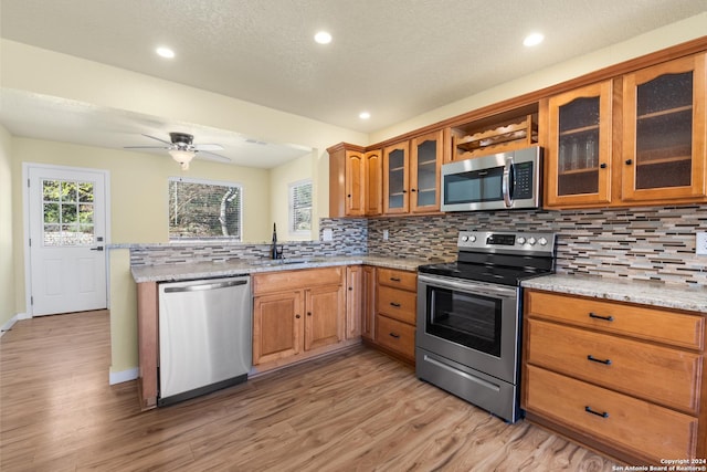 kitchen with sink, decorative backsplash, light hardwood / wood-style floors, light stone counters, and stainless steel appliances