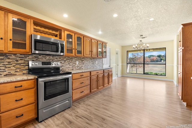 kitchen with an inviting chandelier, light hardwood / wood-style flooring, tasteful backsplash, light stone counters, and stainless steel appliances