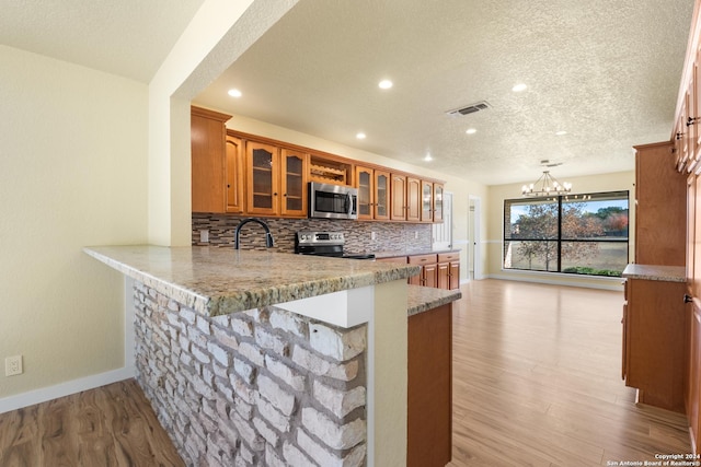 kitchen with kitchen peninsula, an inviting chandelier, stainless steel appliances, and light wood-type flooring