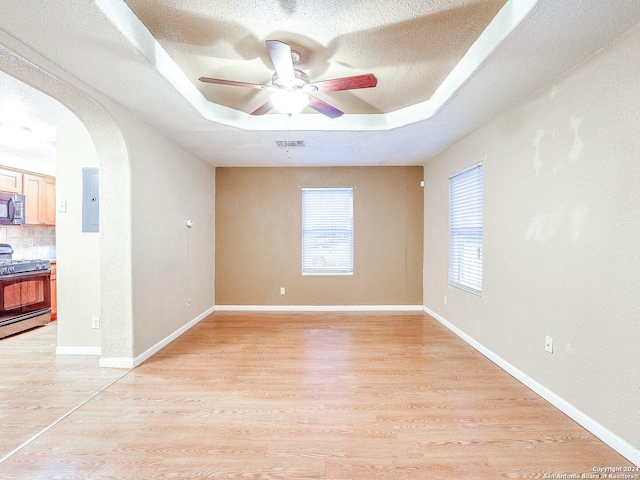 unfurnished room with electric panel, ceiling fan, light wood-type flooring, a textured ceiling, and a tray ceiling