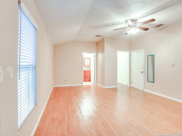 empty room with vaulted ceiling, ceiling fan, a textured ceiling, and light wood-type flooring